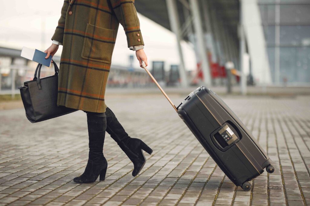 Stylish woman with suitcase and bag walking on street near modern airport terminal| Luxylounge

